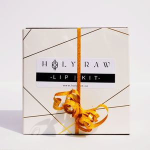 The Holy Raw lip kit off white box with a gold ribbon and abstract metallic gold lines across the box