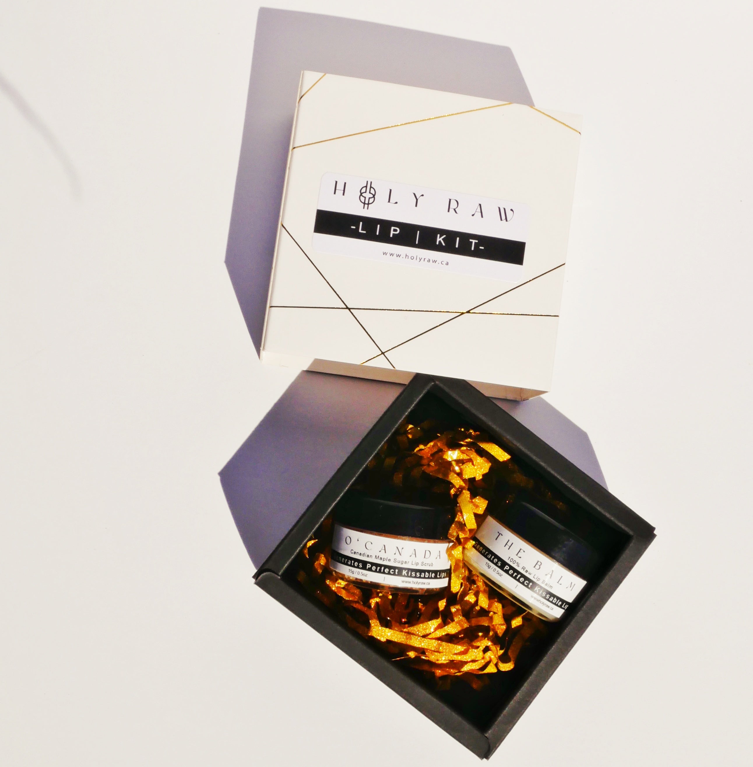 The holy raw lip kit sliding draw box opened displaying its contents which contains both the o'canada maple sugar lip scrub and the balm lip balm surrounded by gold confetti.